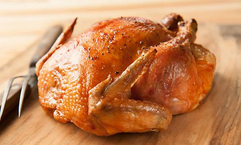 Classic Roast Chicken sits next to kitchen utensils on a wooden table.