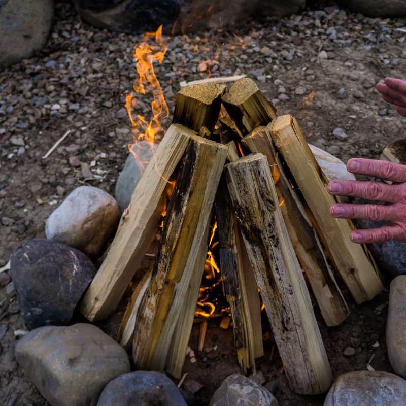 A man warms his hands on a campfire that is encircled by stones.