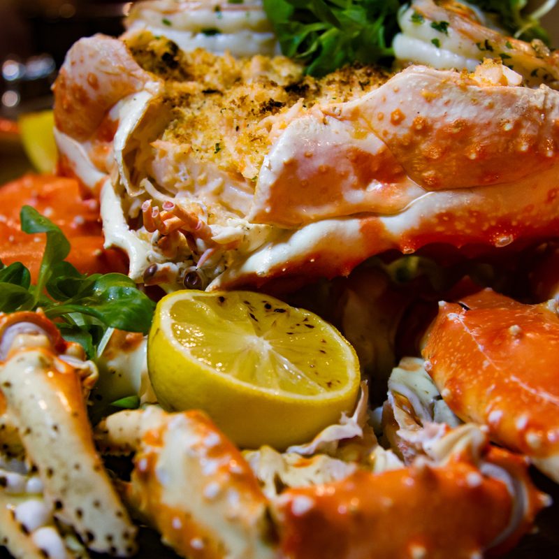 A close-up of a crab with lemon and greens.