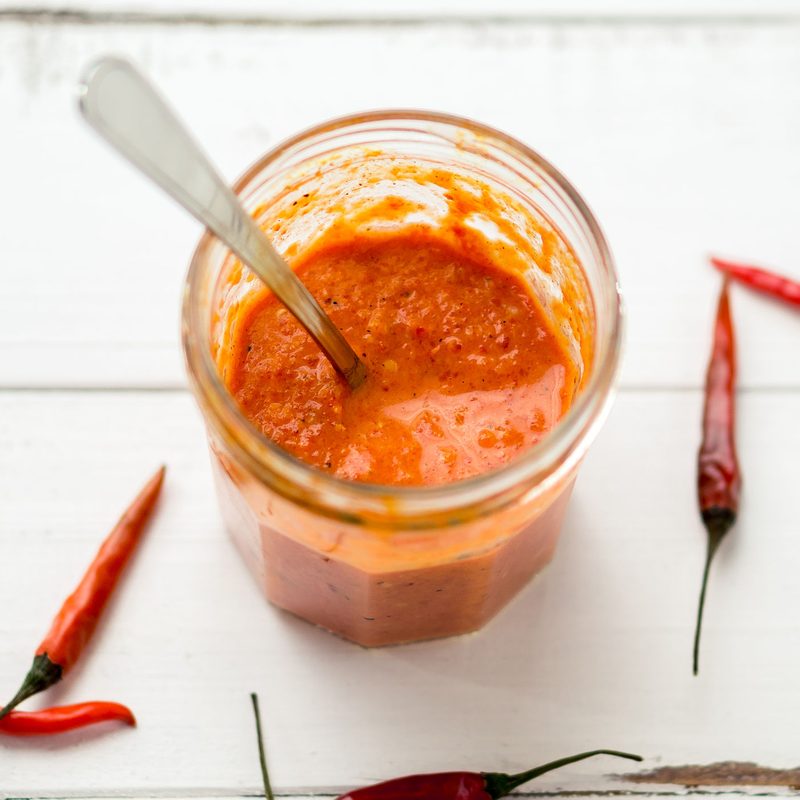 Homemade hot sauce in a jar with small red chili peppers on the side.