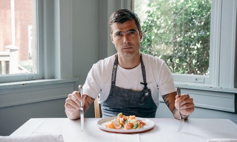 hugh acheson celebrity chef with fork and knife in hand and dinner plate at table