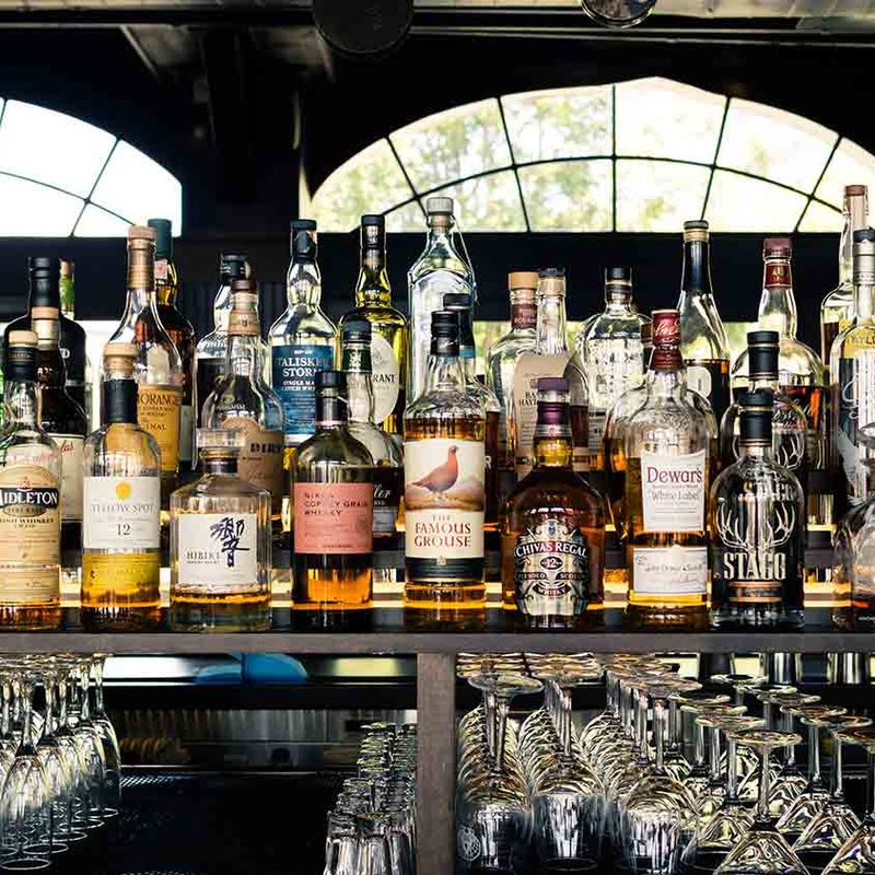 An assortment of liquor bottles line a bar shelf.