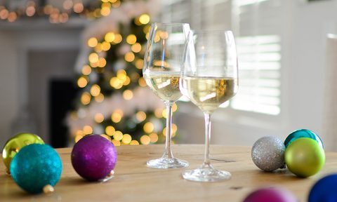 Two glasses of wine and Christmas balls on a table in a room with Christmas tree.