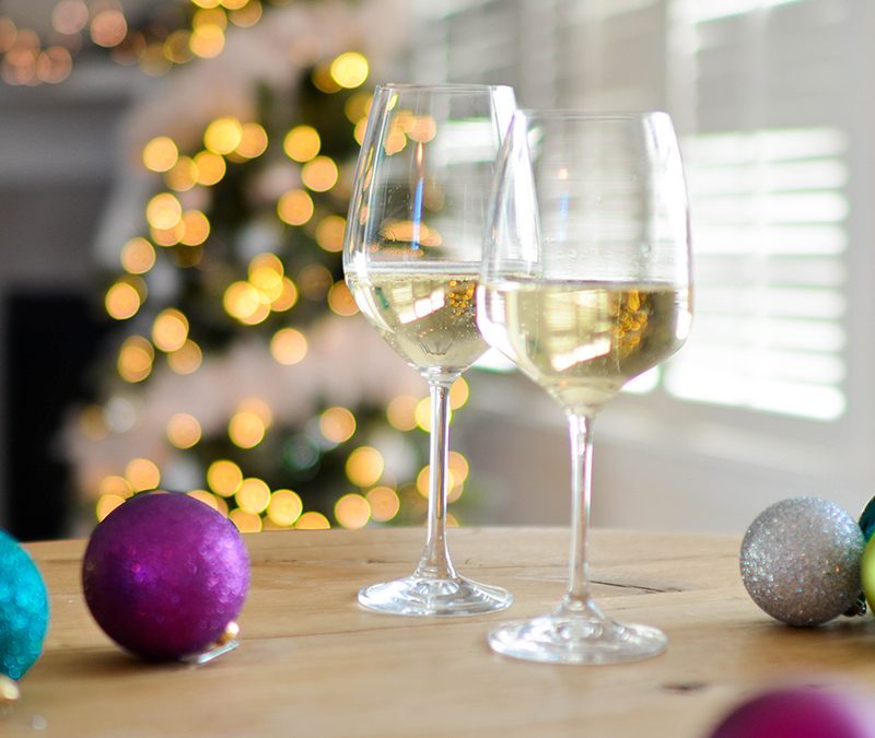 Two glasses of wine and Christmas balls on a table in a room with Christmas tree.
