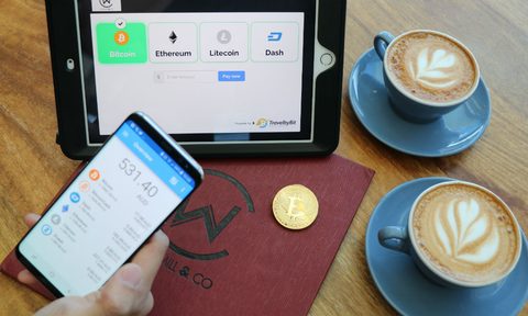A Bitcoin is pictured next to a cell phone, iPad and two cups of coffee.