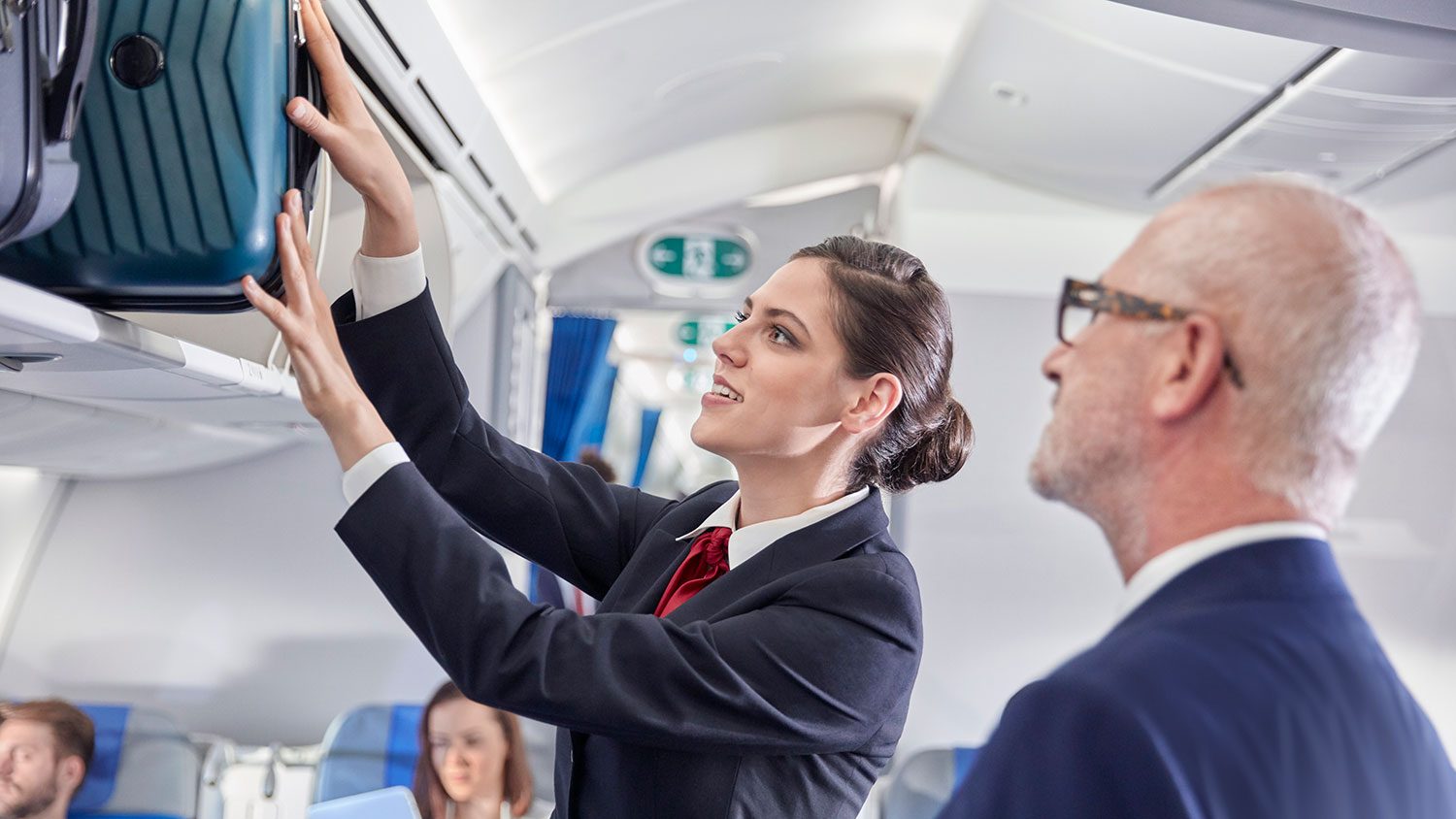 Flight attendant helping businessman place luggage in overhead compartment on airplane