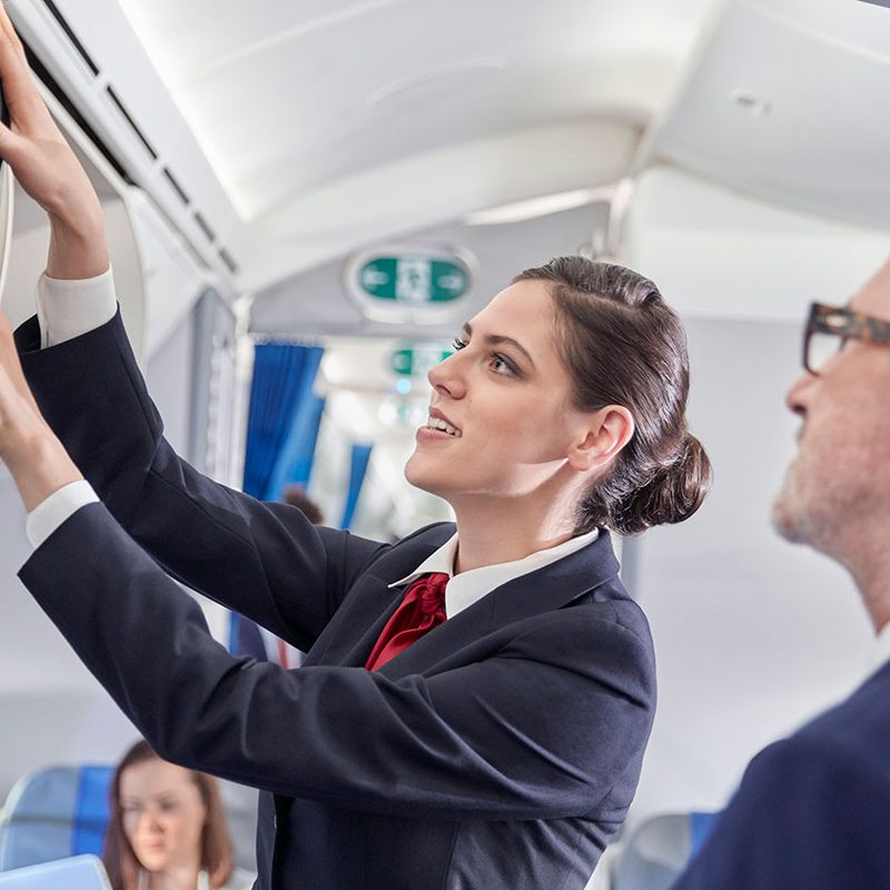 Flight attendant helping businessman place luggage in overhead compartment on airplane