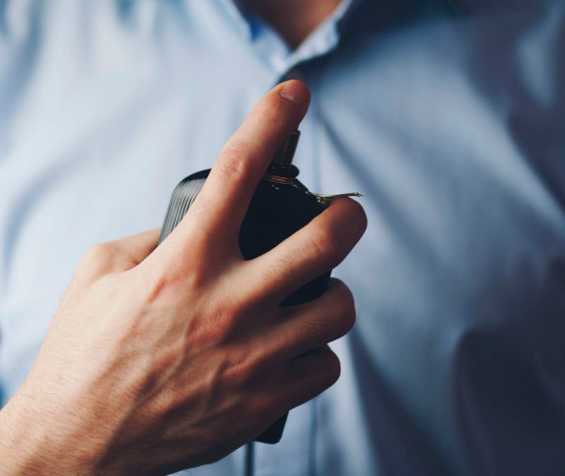 Man spraying cologne wearing a blue shirt