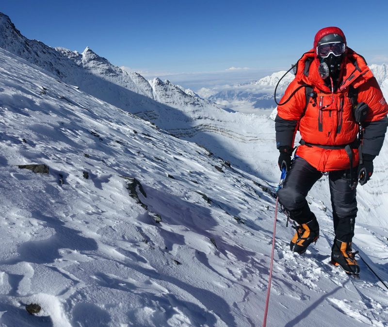 A climber in a red parka with supplemental oxygen on their way up Mount Everest.