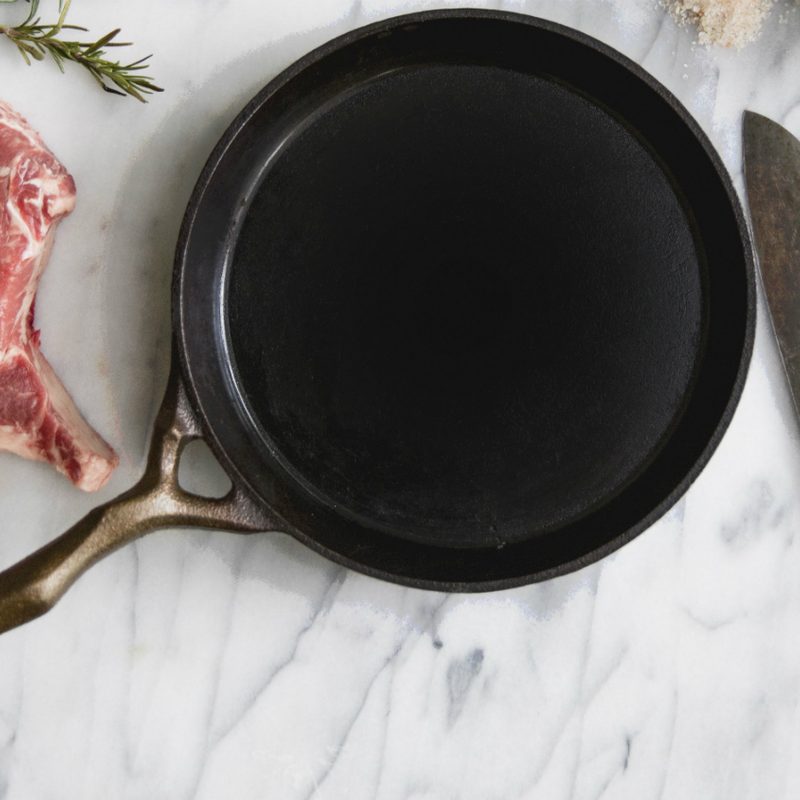 Cast iron skillet on marble slab with steak and knife.