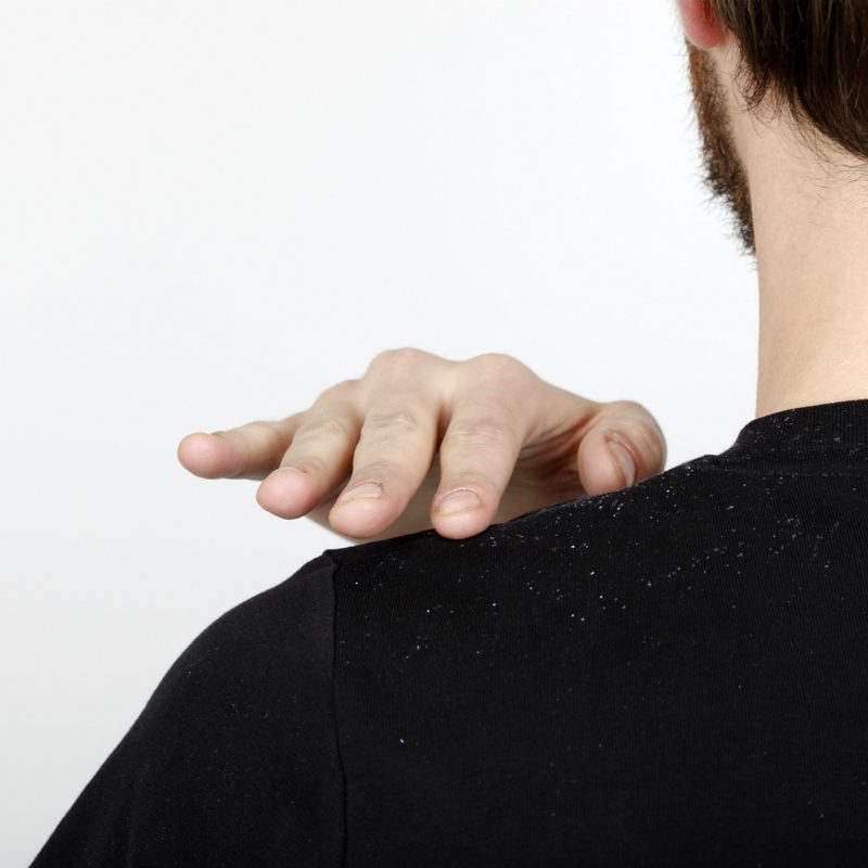 Man brushing away dandruff from his black shirt.