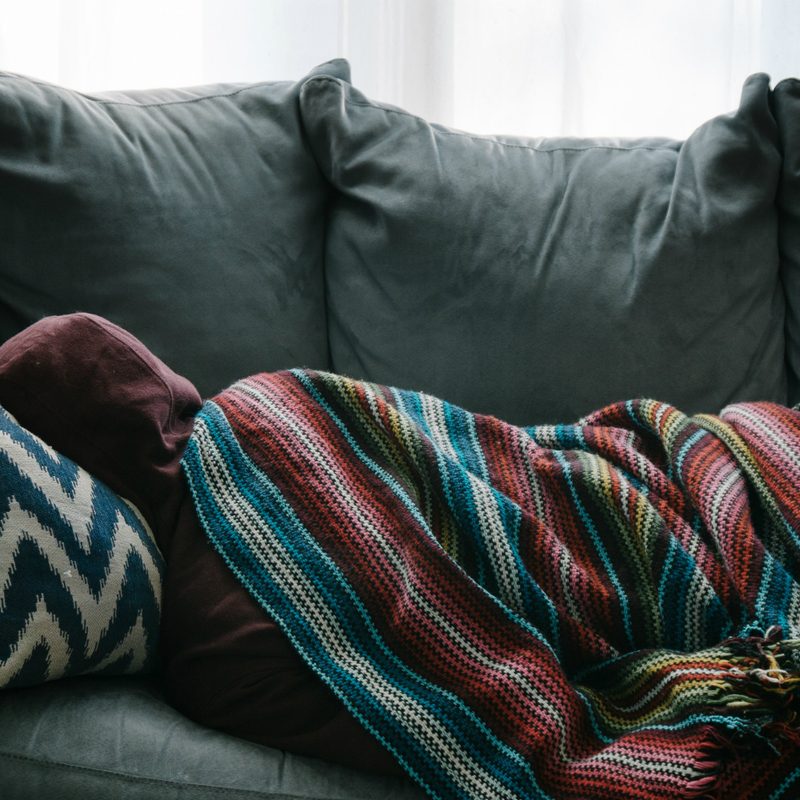 A person curled up sick on a couch.
