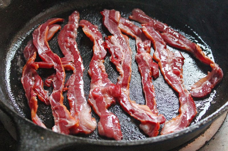 Strips of bacon being cooked in a pan.