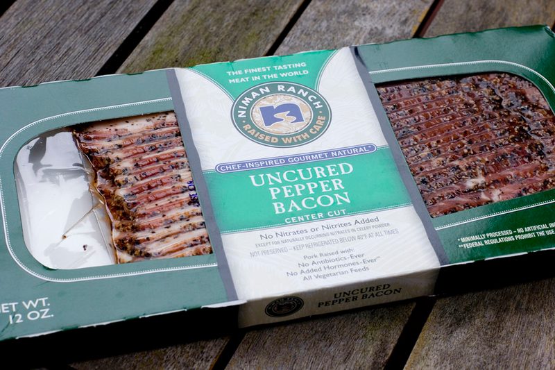 A rectangular box of uncured pepper bacon from Niman Ranch on a wooden surface.