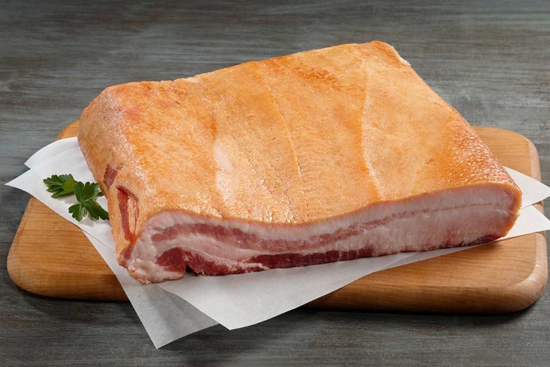 An herb and a slab of bacon on absorbing paper placed on top of a wooden cupboard.