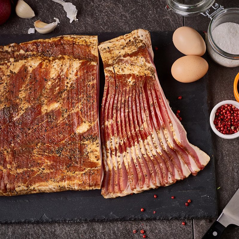 A knife, slab of sliced raw bacon, egg, and other ingredients.
