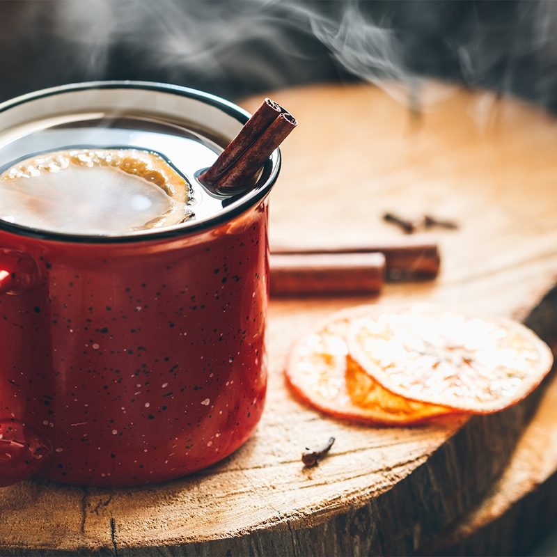 steaming cup of hot toddy sitting on a wood block cutting board.