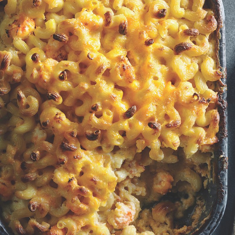 Kitchen Toke Cannabis Infused Lobster Mac and Cheese in a casserole dish sitting next to a wooden spoon.