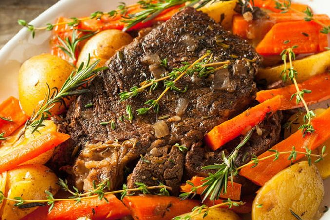 Pot roast with carrots and potatoes in baking pan.