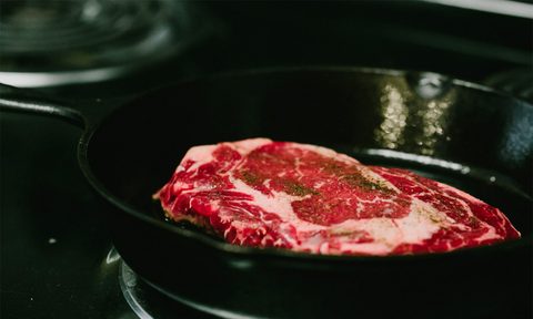Ribeye steak cooking in a cast iron pan