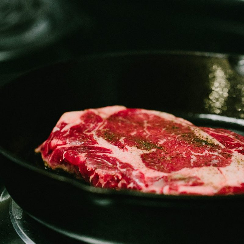 Ribeye steak cooking in a cast iron pan