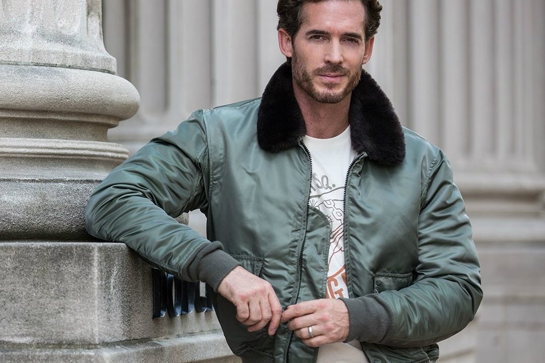 A man wearing a bomber jacket under a white shirt.