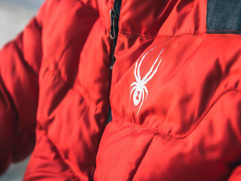Closeup of white Spyder logo on a red ski jacket.