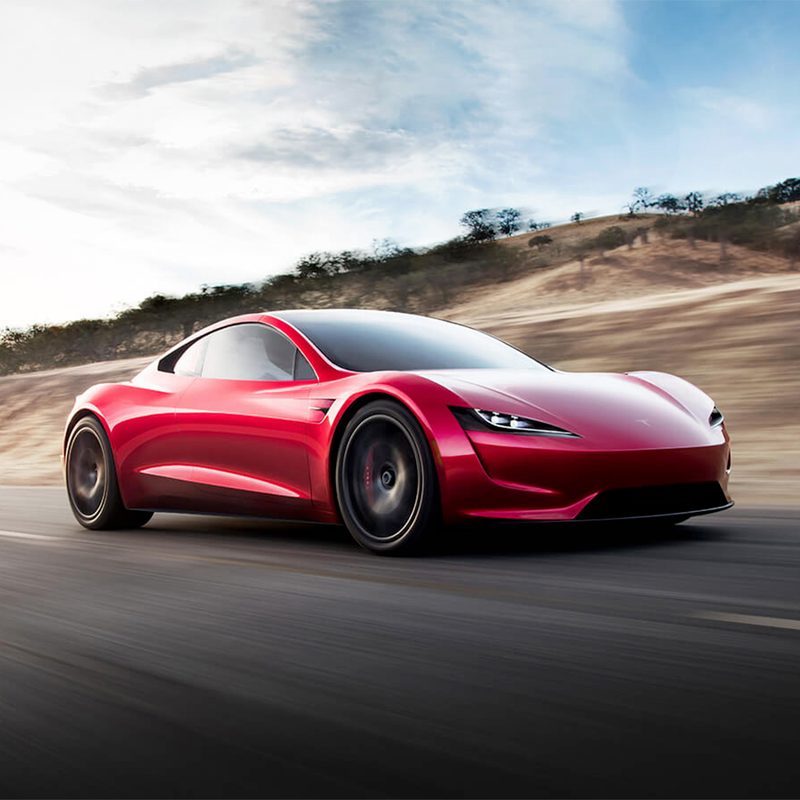 Red Tesla Roadster speeding down a freeway with a blurry background.