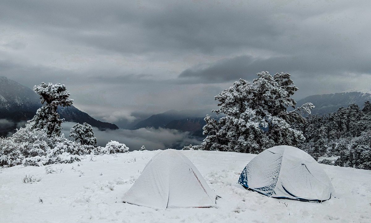 Two camping tents covered in snow on a mountain in winter.