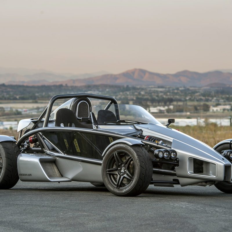 Ariel Atom 3RS open-air sports car parked on pavement with desert mountains in the background.