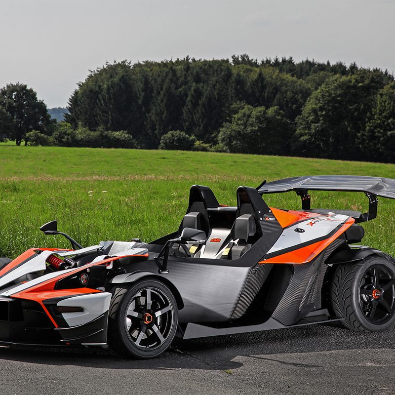 Wimmer-RST KTM X-Bow GT parked on pavement near a green open field.
