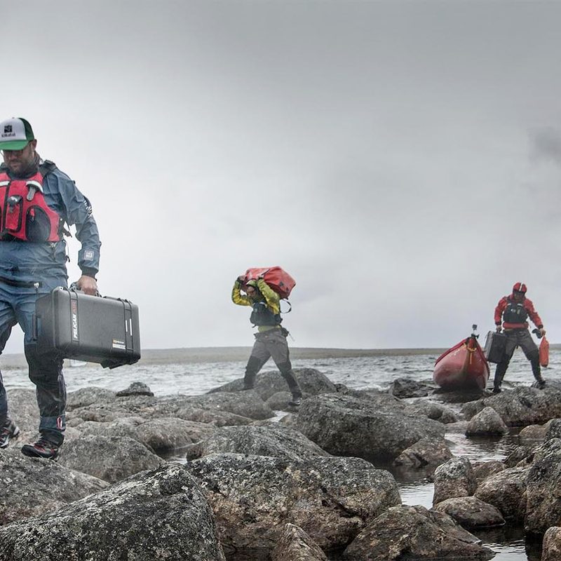 Paddlers standing on boulders near the ocean with their outdoor gear in Pelican cases