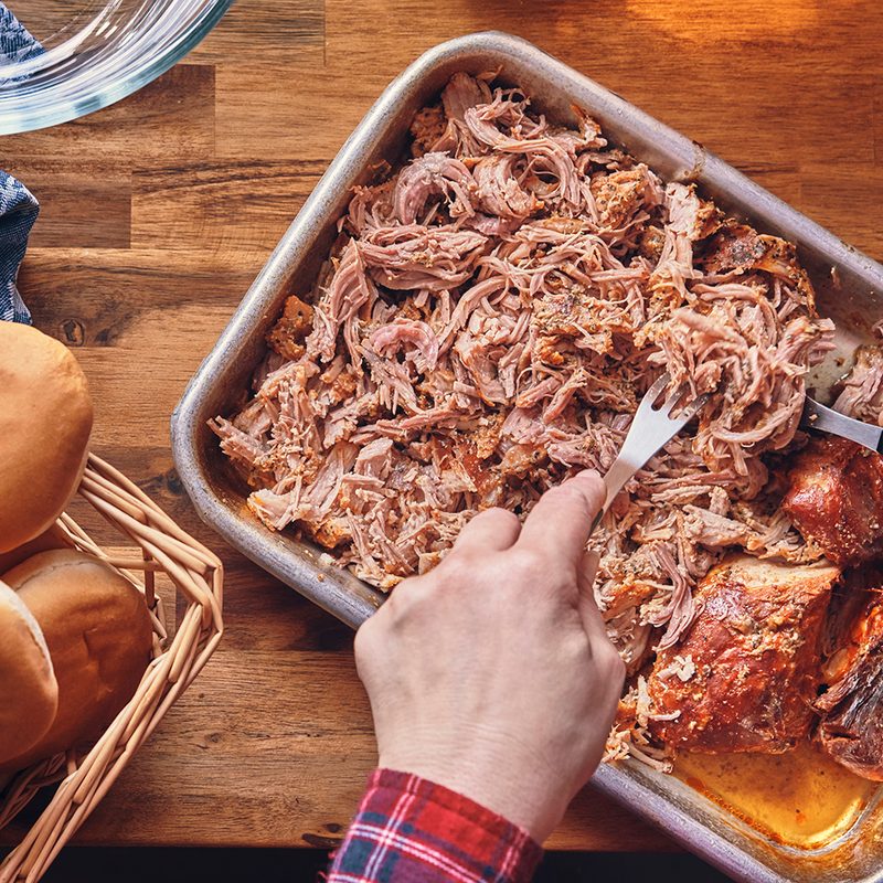 Man shredding pulled pork in a pan.