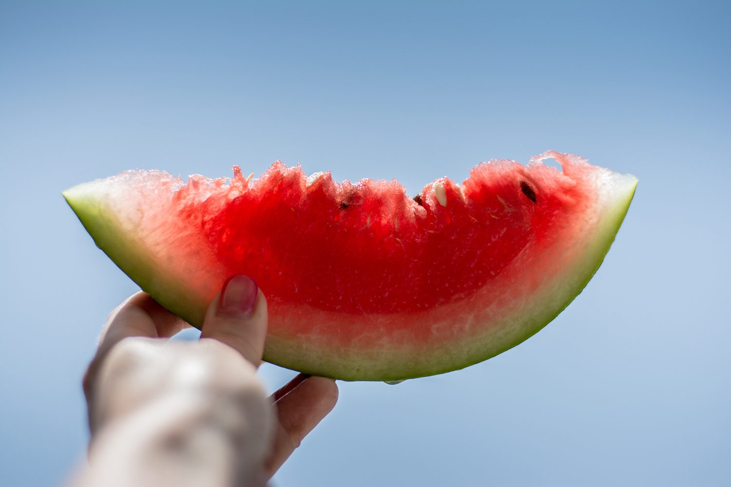 Watermelon slice being held up in the air outside.