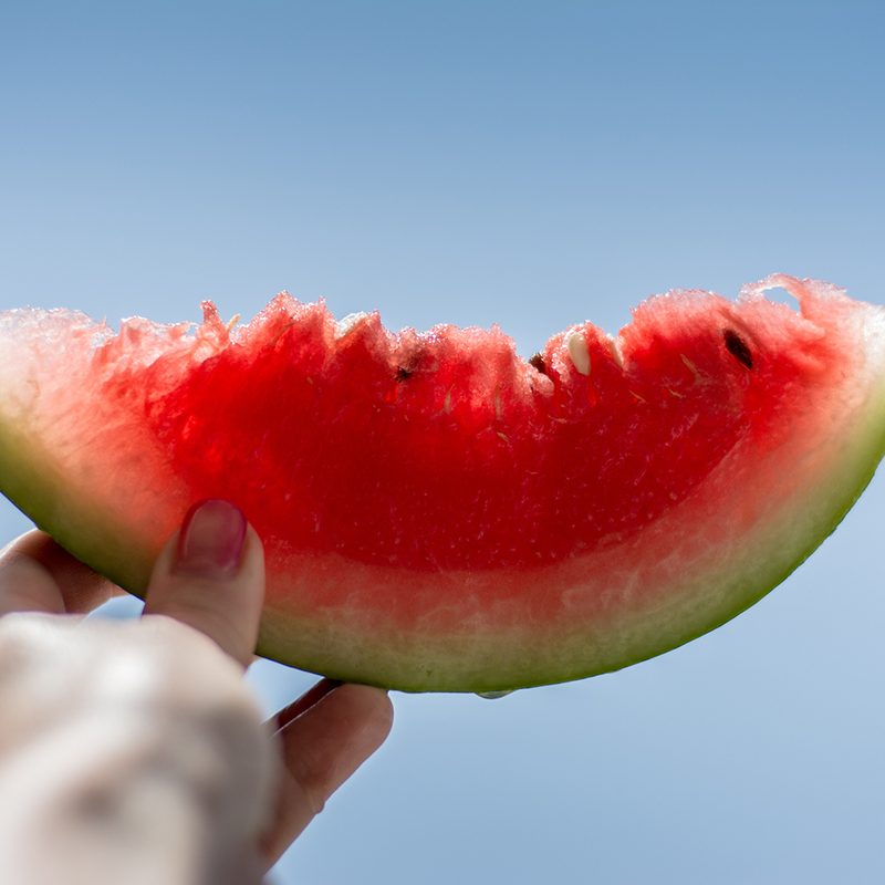 Watermelon slice being held up in the air outside.
