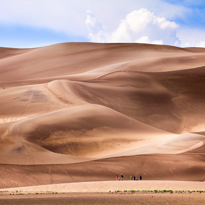 Wide-angle shot of people standing in front of large dunes at Great Sand Dunes National Park.