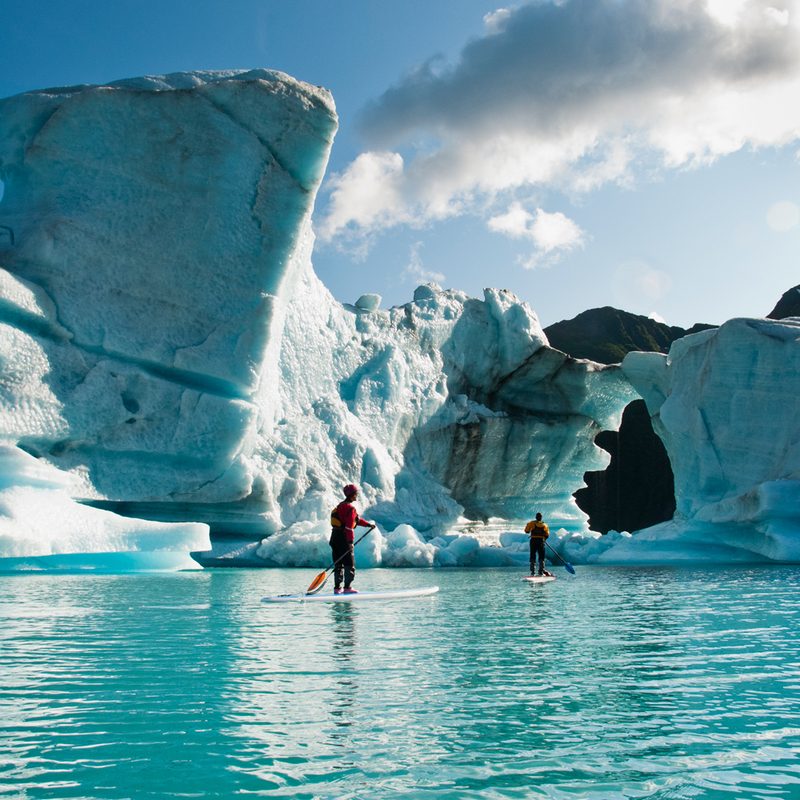 Two people paddleboarding among glaciers in Alaska's Kenai Fjords National Park.