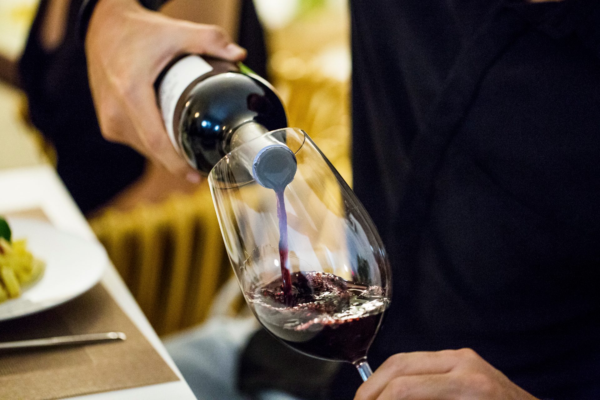 Man pouring red wine in glass during dinner party