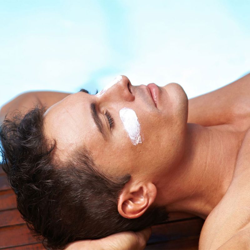 Man laying by a pool with sunscreen under his eyes