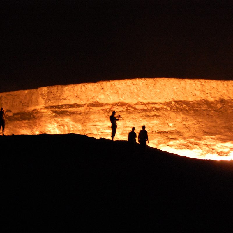 People in silhouette standing in front of Turkmenistan's "Gates of Hell."