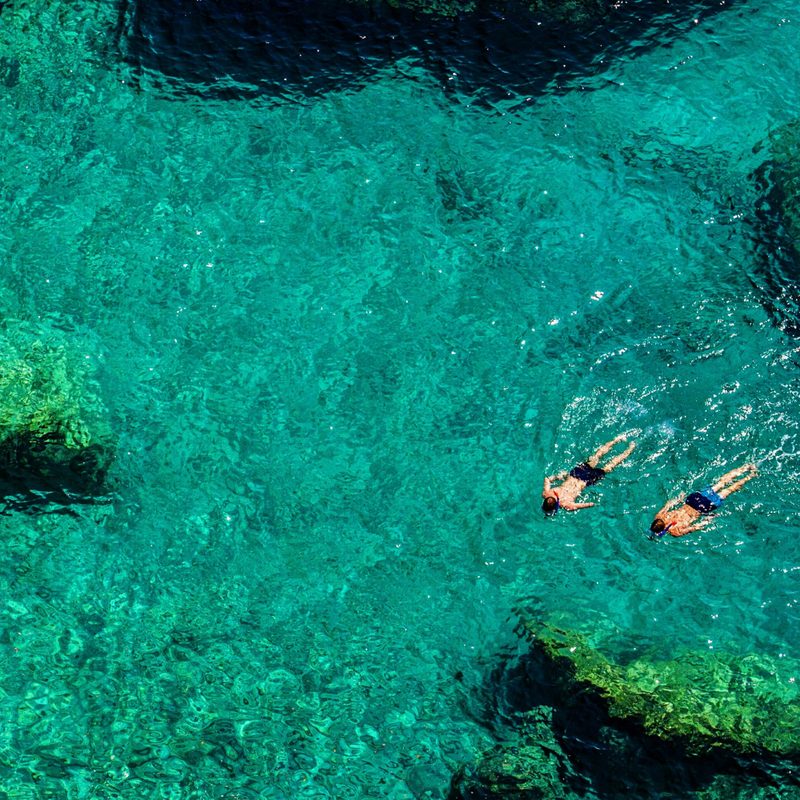 Aerial view of two men snorkeling in clear, shallow tropical water.