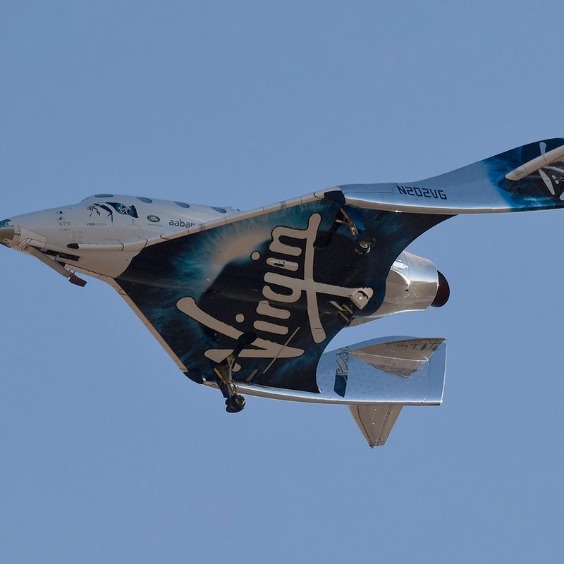 Virgin Galactic aircraft in flight against a clear blue sky.