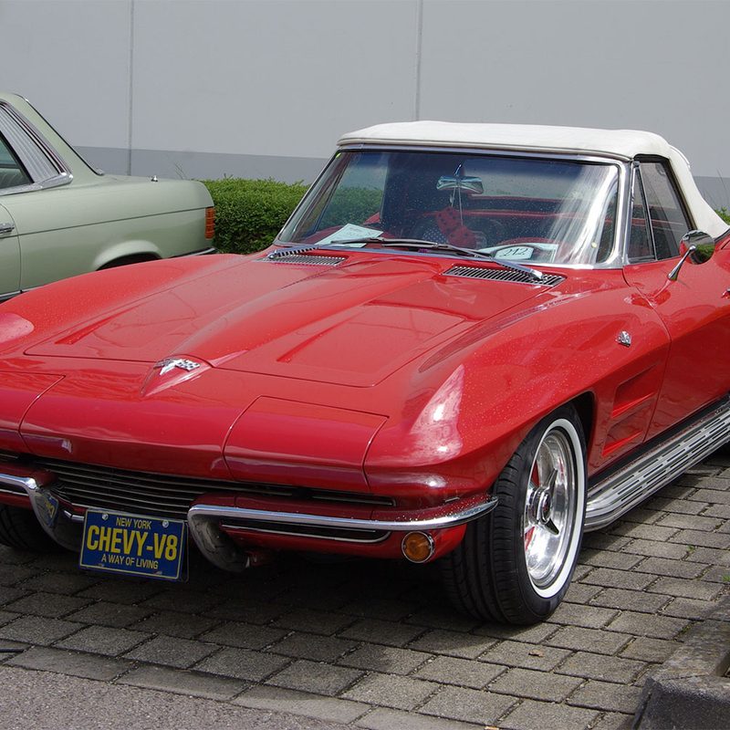 Red classic Chevy Corvette sitting in a parking lot.