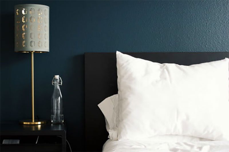 A bed with a white pillow beside a nightlamp.