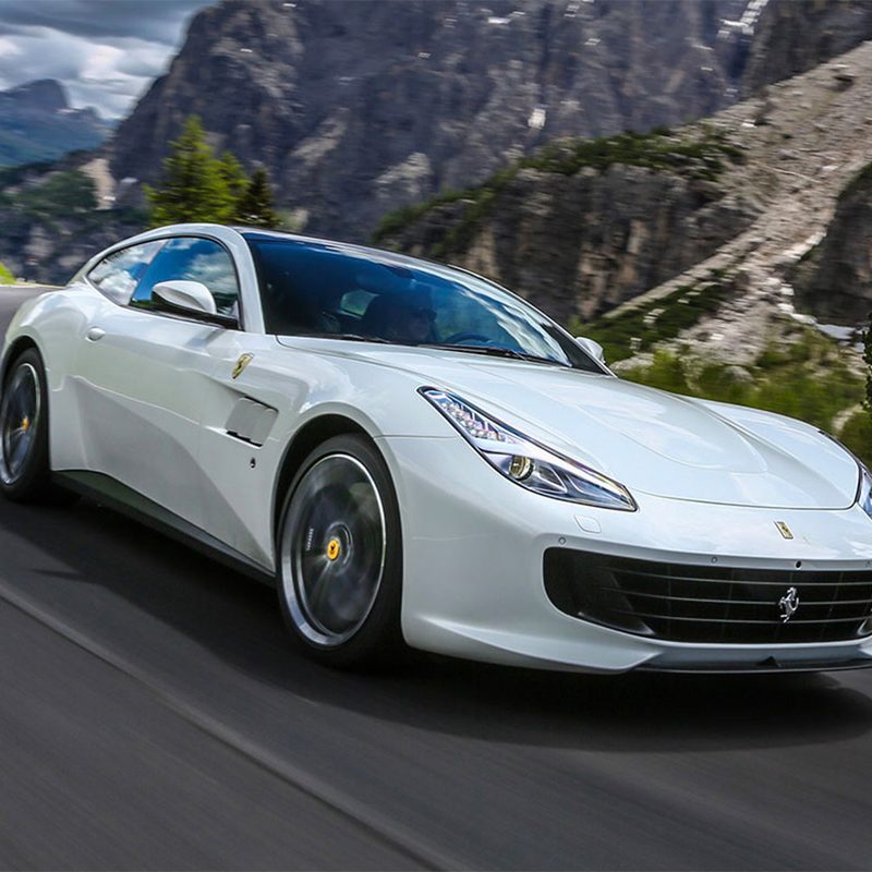 White Ferrari GTC4Lusso driving on a curvy road with trees blurred in the back.