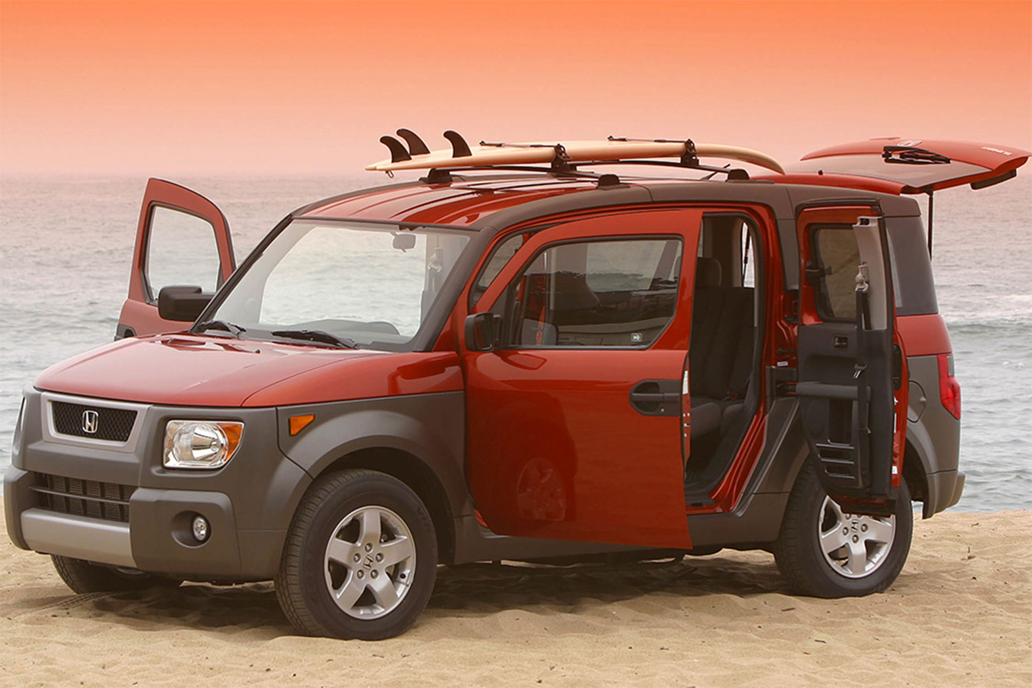 Red Honda Element parked with all its doors open on a beach during sunset.