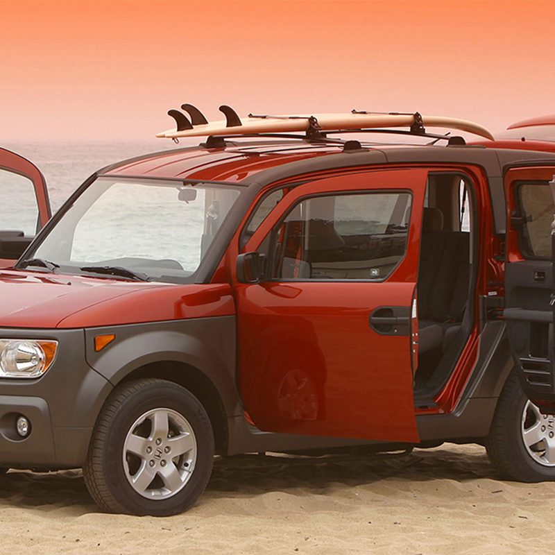 Red Honda Element parked with all its doors open on a beach during sunset.
