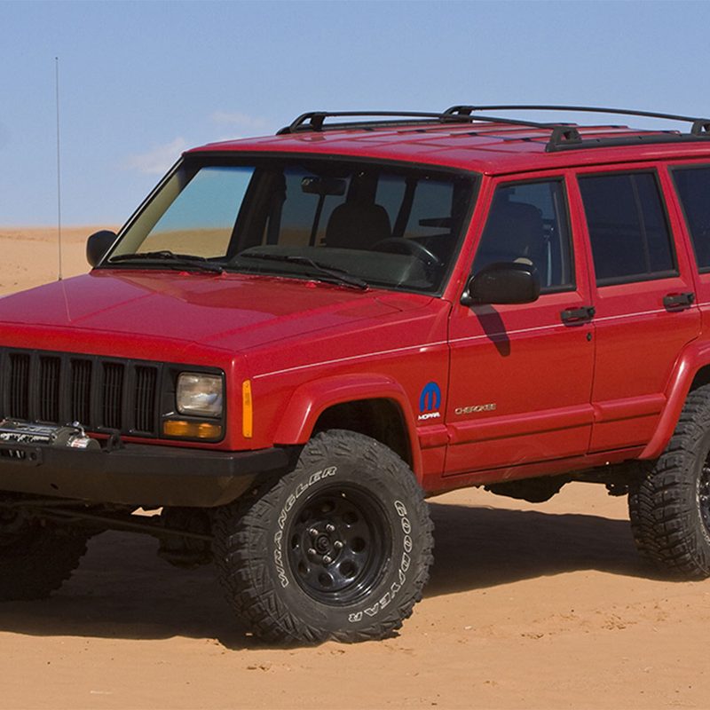 Red Jeep Cherokee XJ parked on a desert in front of a blue sky.
