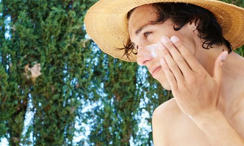 Man applying sunscreen to face with straw hat