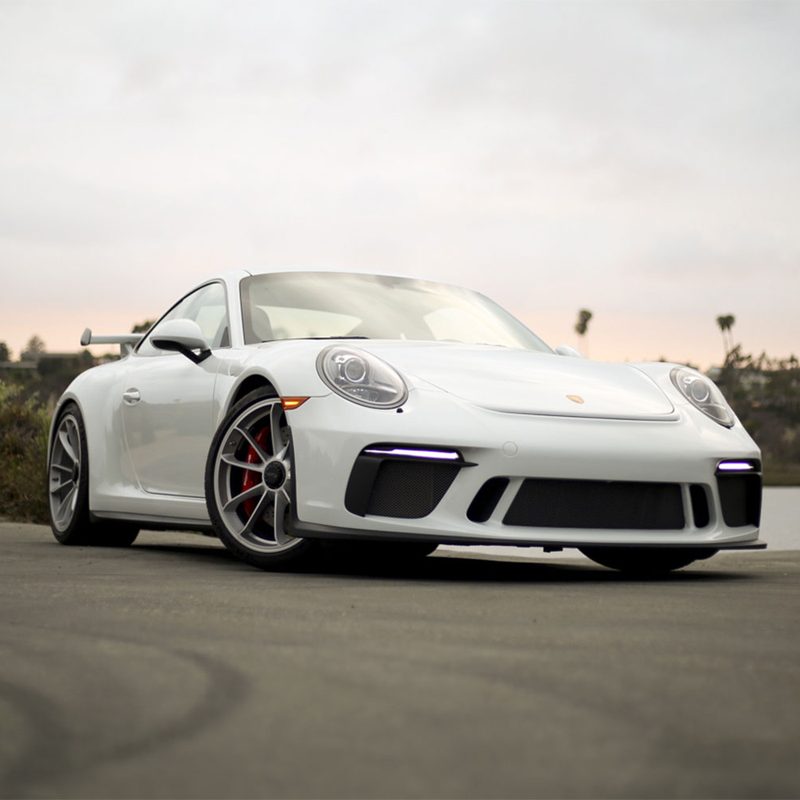 White Porsche 911 front end from the ground on asphalt in sunset.